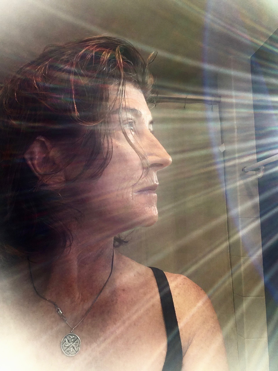 A woman looking at the sun through a window.
