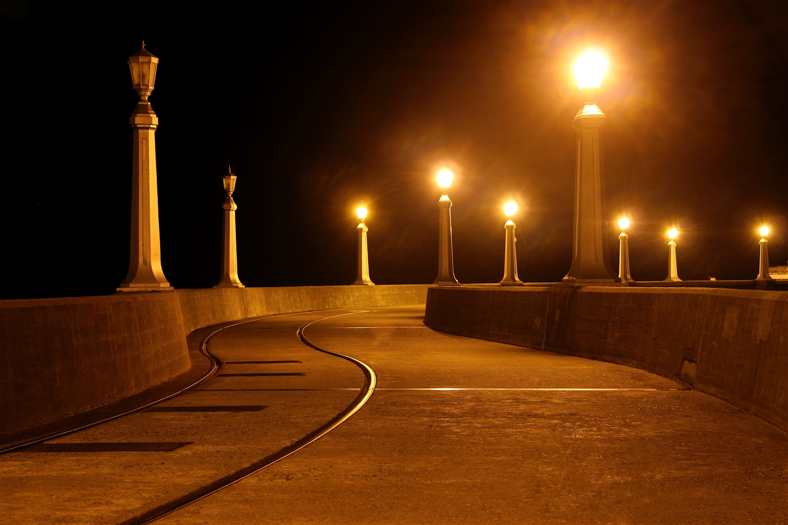 A sidewalk with light poles and a train track.