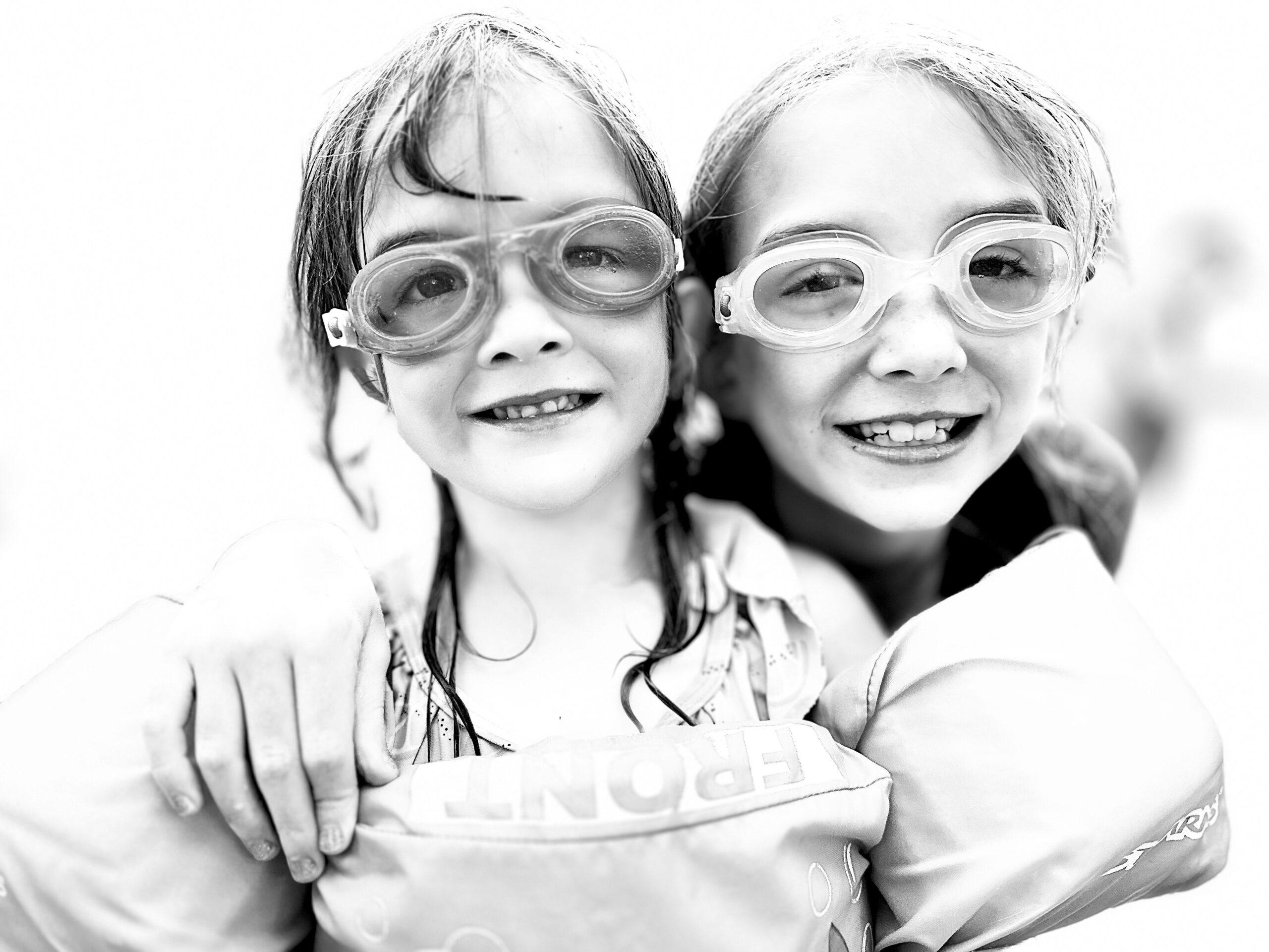 Two girls with goggles and swimsuits posing for a photo.