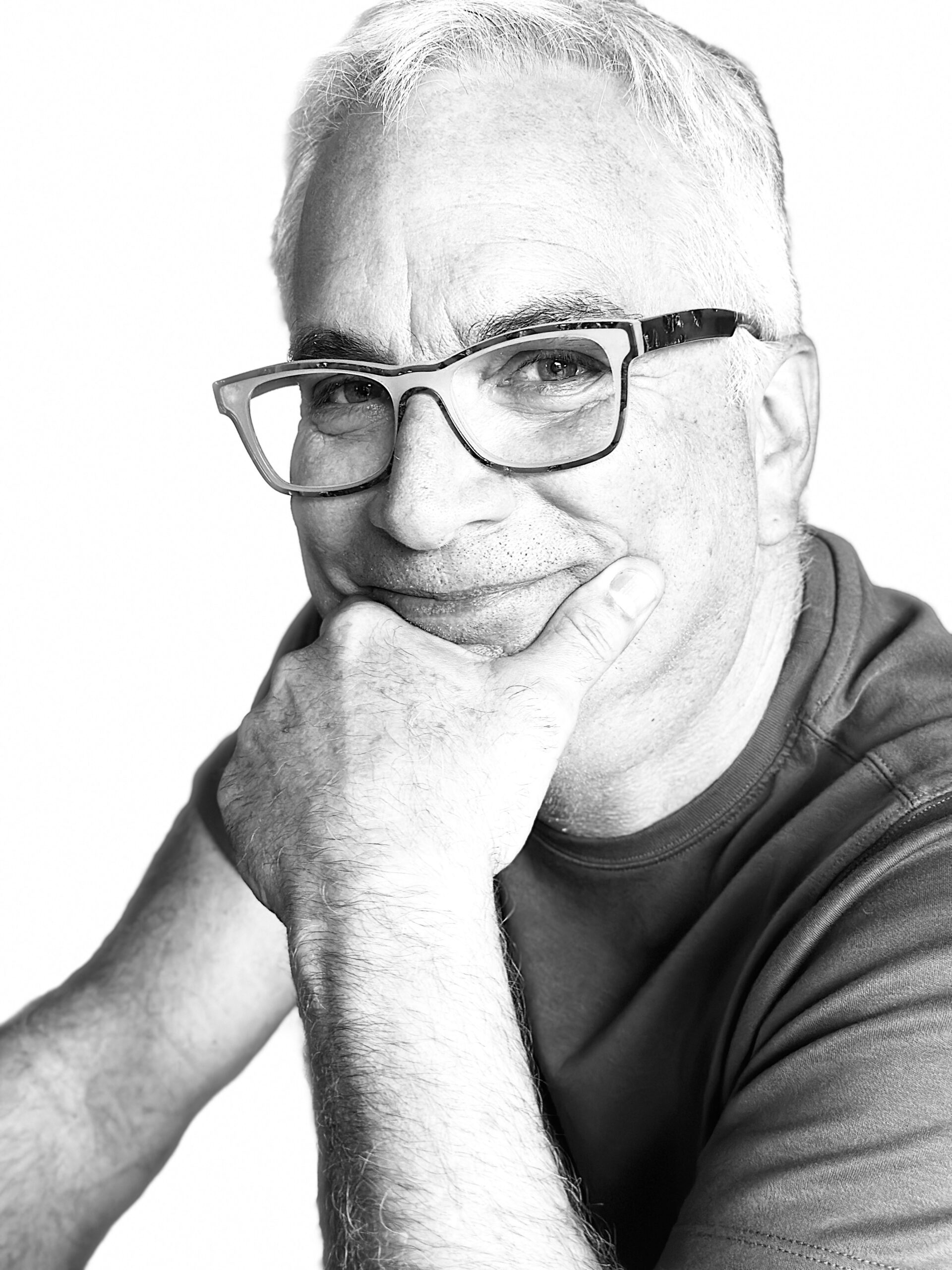 A man in glasses is posing with his hand on his chin.