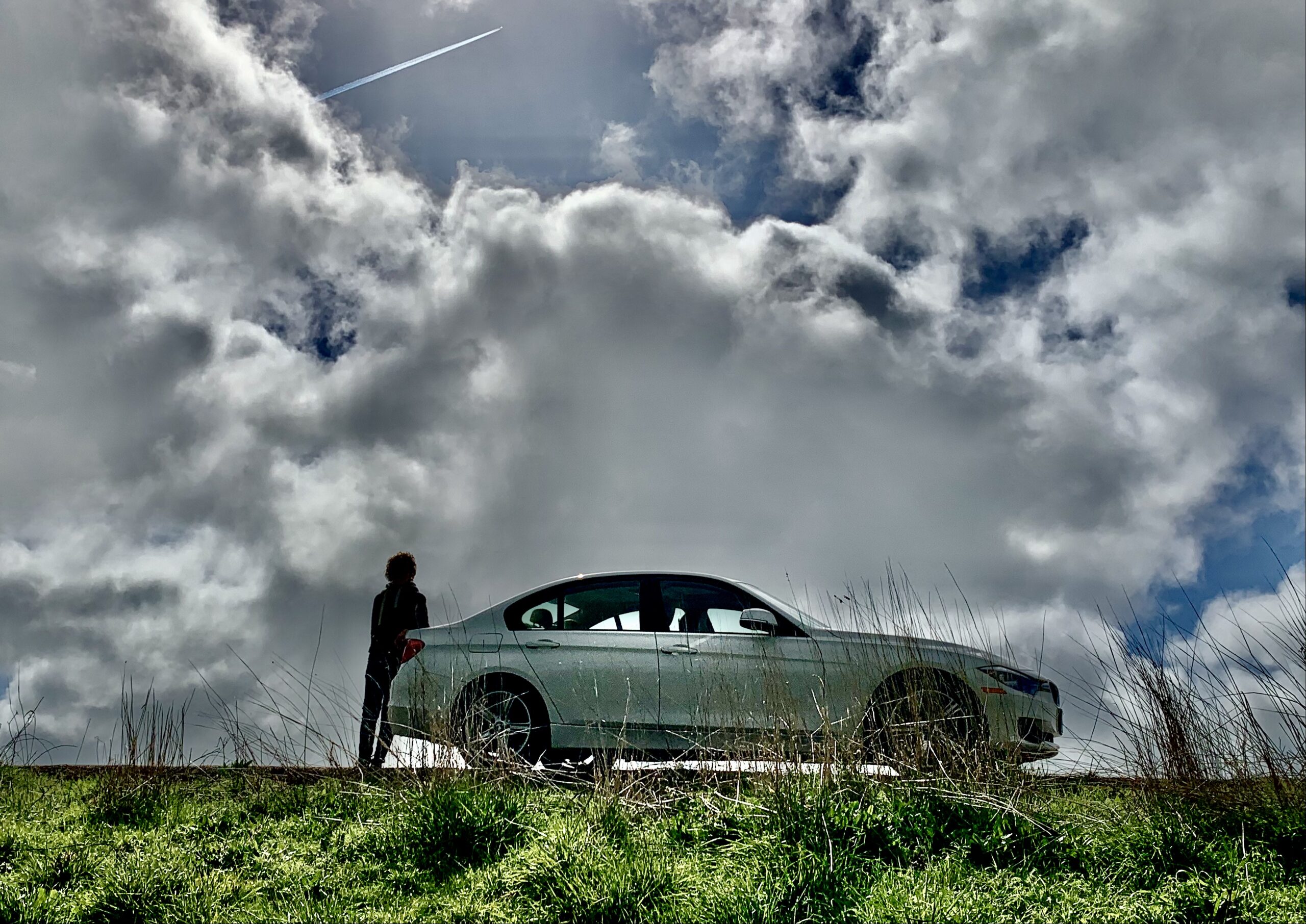 A person standing next to a white car under a cloudy sky.