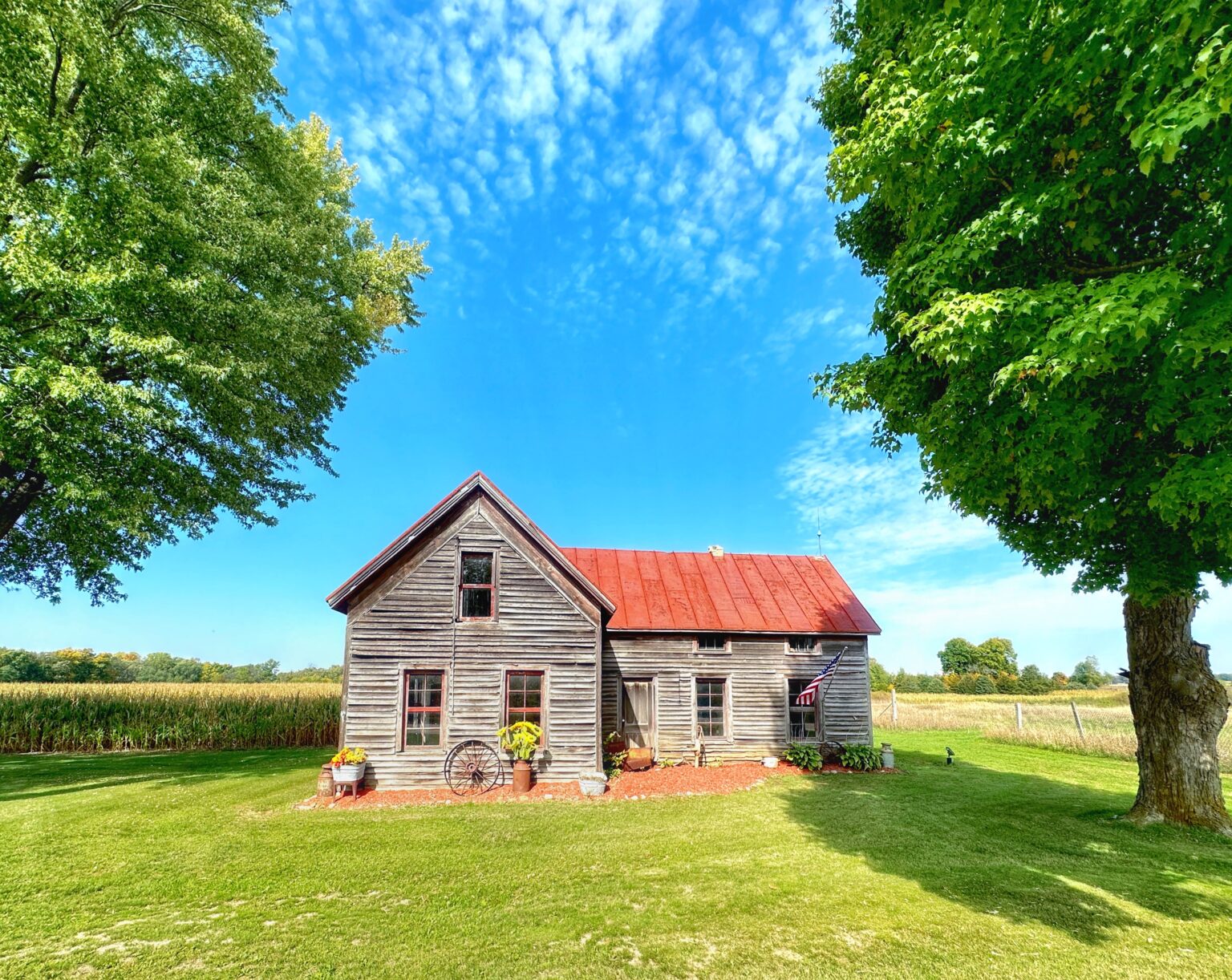 An old farmhouse with a red roof in the middle of a field.